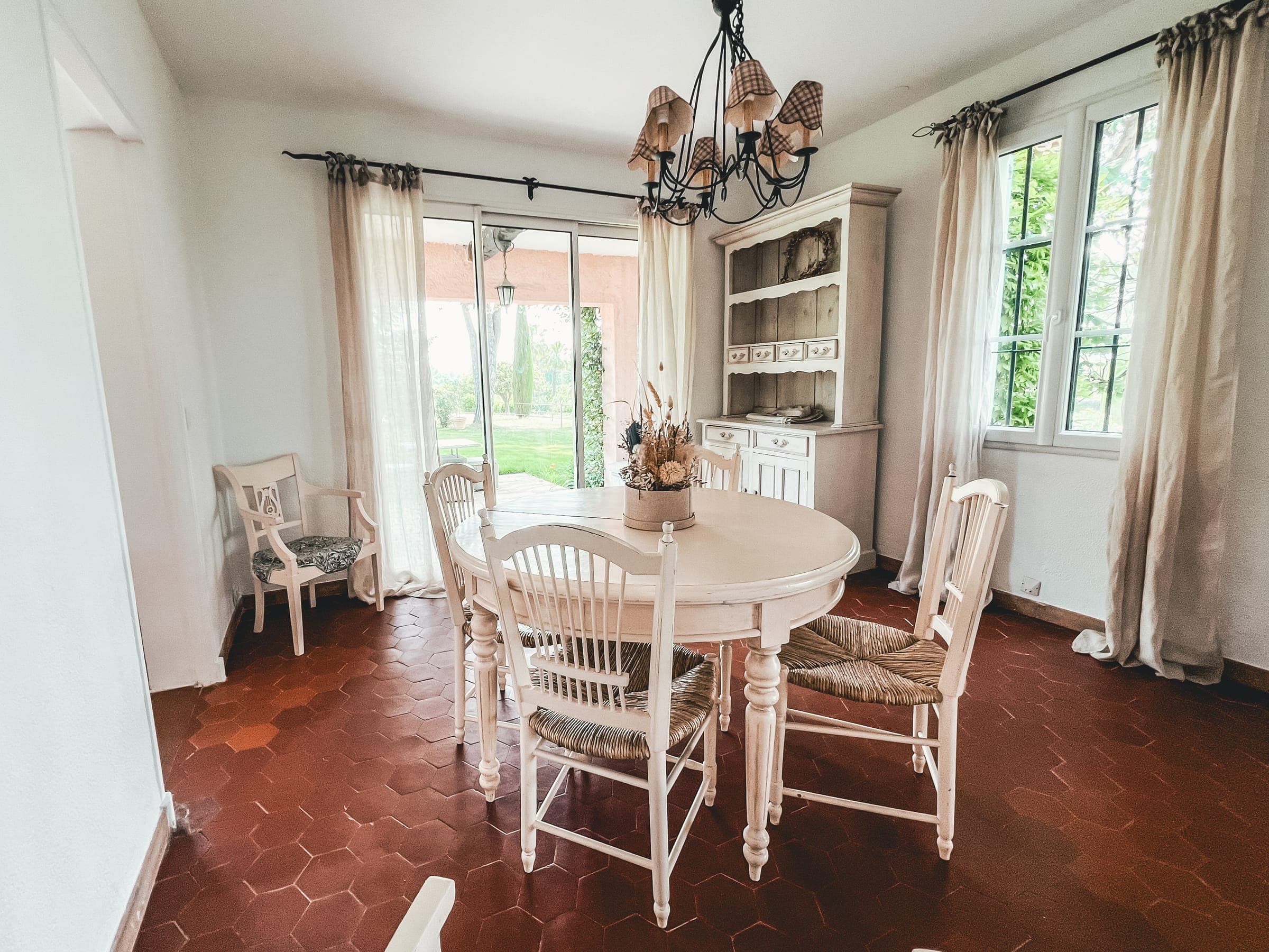 Salle à manger lumineuse avec table ronde blanche, chaises paillées et lustre