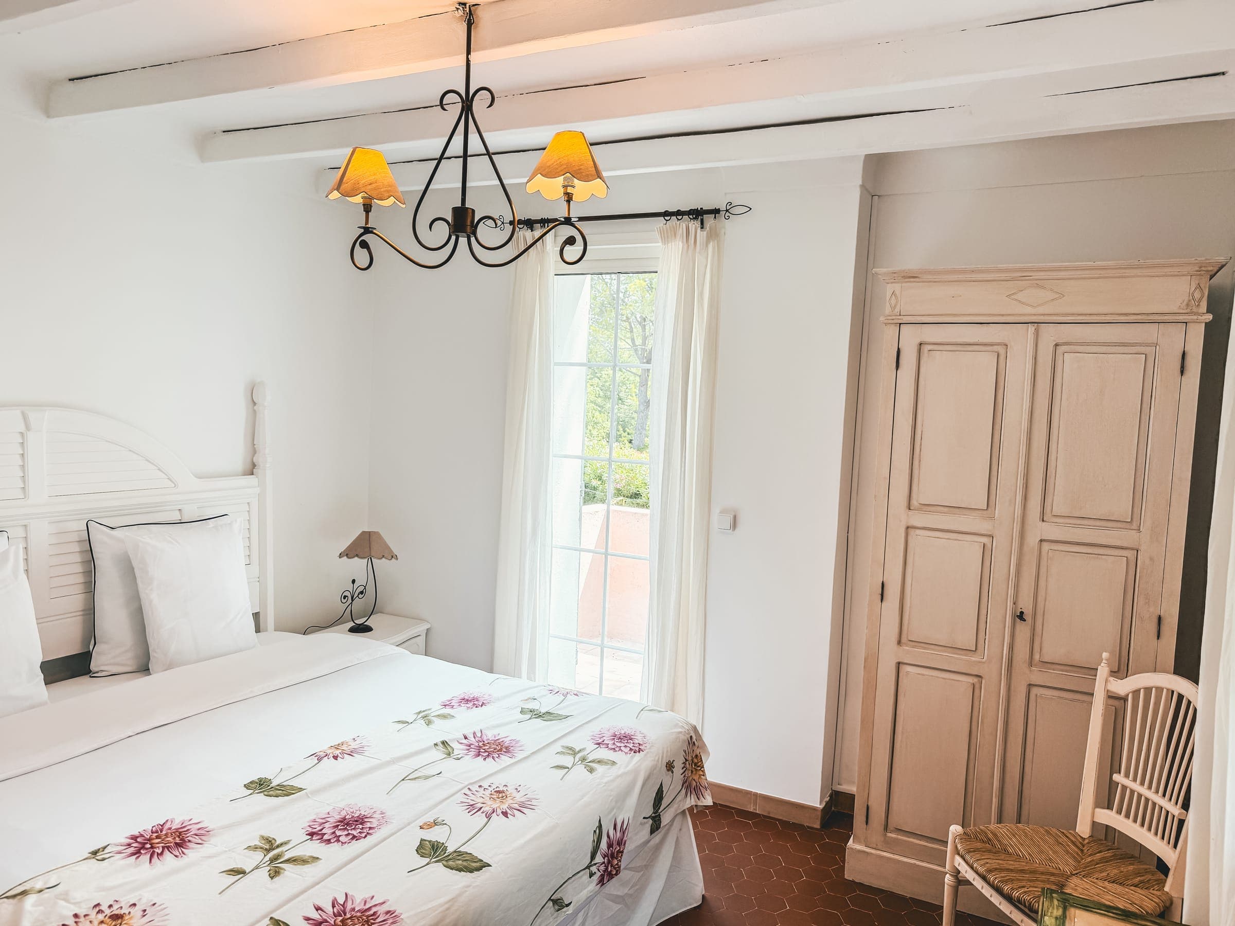 Chambre parentale avec couvre-lit fleuri, plafond à poutres et porte sur la terrasse